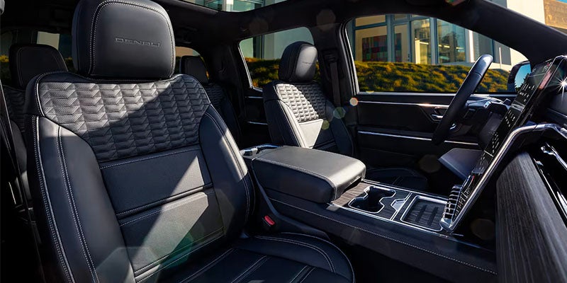 
Interior of a vehicle showing black quilted leather seats and a center console with wood trim.